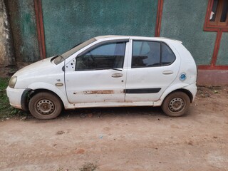 An old white car near a building needs to be repaired