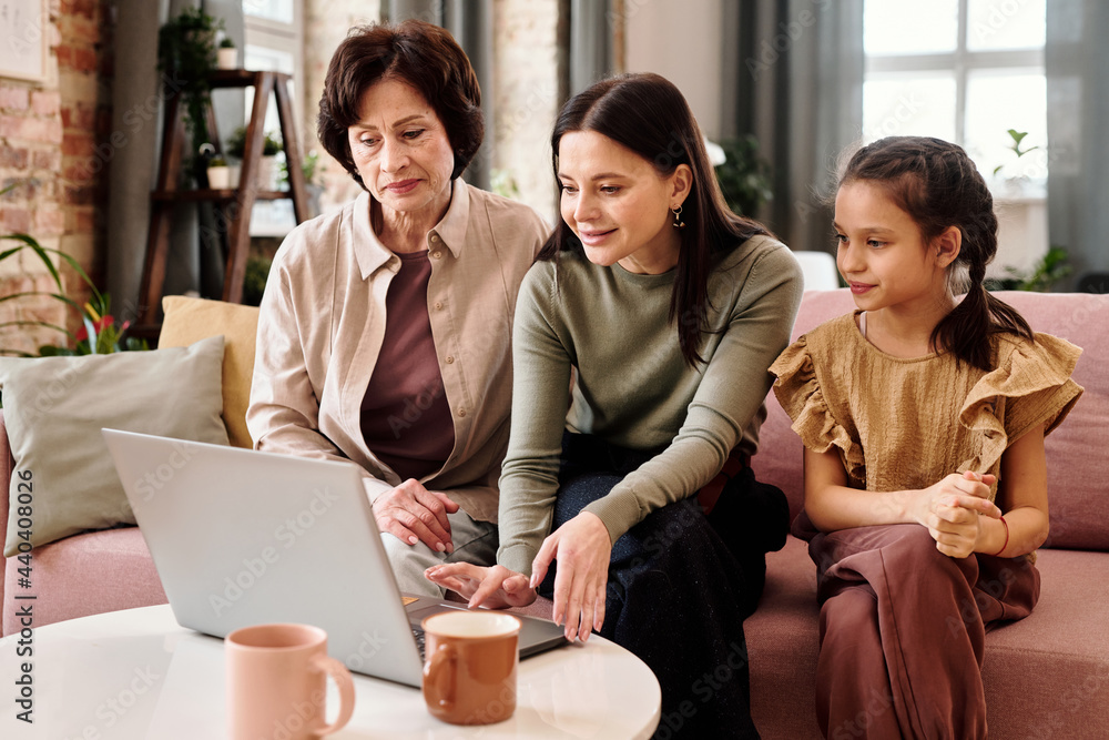 Sticker Two women and little girl sitting on sofa in front of laptop during video call