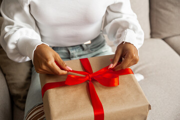 Christmas lifestyle and shopping and black friday concept. Close up hands of african american young woman opens box with christmas gift with red ribbon.