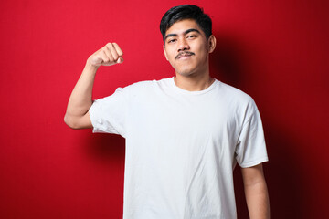 Young handsome asian man wearing white tshirt showing arms muscles smiling proud. fitness concept.
