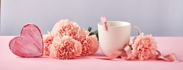 Bouquet of pink carnations and white cup. Design concept of holiday greeting with carnation bouquet on pink and blue background