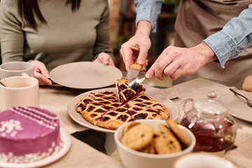 Young man in apron taking piece of tasty homemade berry cake