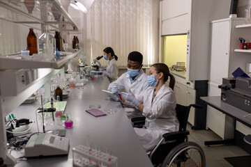 Naklejka premium Caucasian female chemist showing her African colleague flask with purple fluid