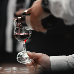The waiter serves rose, red and white wine from the wine bottle in the wine glass at an event.