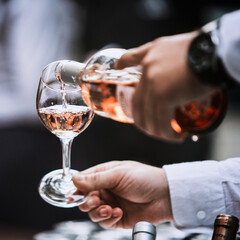 The waiter serves rose, red and white wine from the wine bottle in the wine glass at an event.