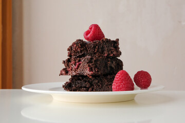 Stack of dark chocolate raspberry brownies on a white plate against light background 