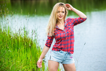The blonde girl is having fun in the river in rubber boots in the country. Young woman on a lake...