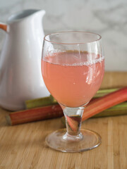 Homemade rhubarb juice in a glass, rhubarbs and a white jar on the background closeup with selective focus