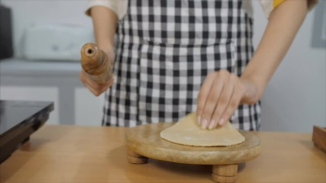 Close up shot of a grown-up woman's hand making fresh chapatis in her kitchen. An Indian woman in an apron rolling and making perfectly round chapatis in her kitchen for her family - lifestyle concept
