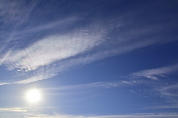 The bright sun hid behind light white clouds in the blue sky.