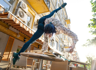 Woman doing handstand on the cafe table with coffee and read a book in cafe outdoor. Concept of...