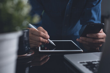 Man Man using mobile phone, and stylus pen on digital tablet during working on laptop computer from...