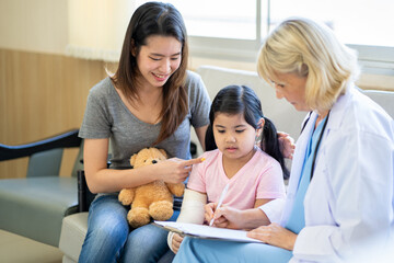 Fototapeta premium Pediatrician doctor examining little asian girl with a broken arm wearing a cast at hospital