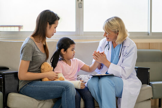 Pediatrician doctor examining little asian girl with a broken arm wearing a cast at hospital