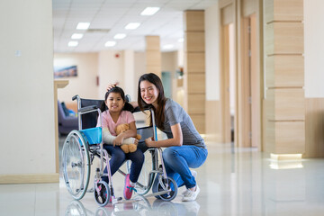 asian girl with a broken arm wearing a cast setting on wheelchair with her mother at hospital