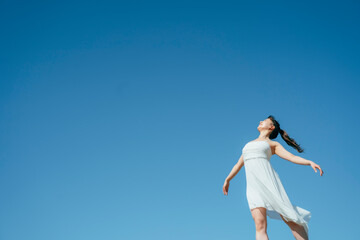 Fototapeta na wymiar 空と白いワンピースの踊る女性（深呼吸・全身） 