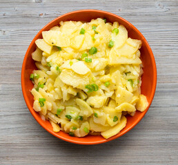 german cuisine - top view of potato salad in orange bowl on wooden table