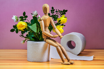 Wooden figure sit on a roll of toilet paper and bouquet of yellow roses on a pink background....