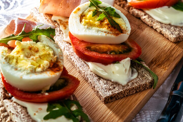 crispbreads with smoked ham, tomatoes and eggs on a cutting board