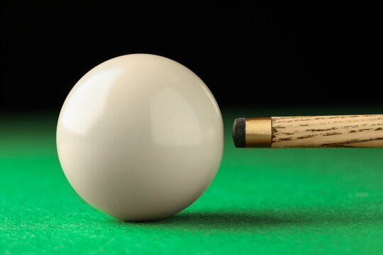 Classic plain billiard ball and cue on green table, closeup