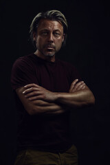 Fototapeta premium Dark portrait of a middle-aged man with blond hair and a gray stubble in a dark brown t-shirt.