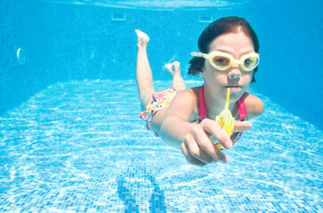 Child swims underwater in swimming pool, active girl dives and has fun under water, kid fitness and sport on family vacation 
