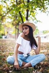 Glamour portrait of a young and beautiful woman sitting in the park. Autumn seasson
