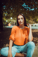 Glamour portrait of a young and beautiful woman sitting in the park. Autumn season