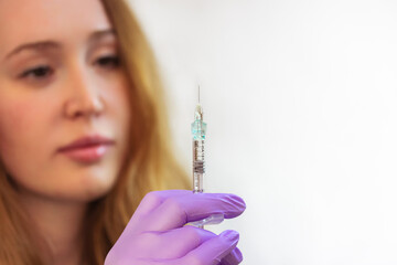 A young woman doctor wearing purple rubber gloves holds an injection syringe with a thin needle. Lip augmentation procedure, facial, body rejuvenation, mesotherapy. Aesthetic cosmetology. Beauty Salon