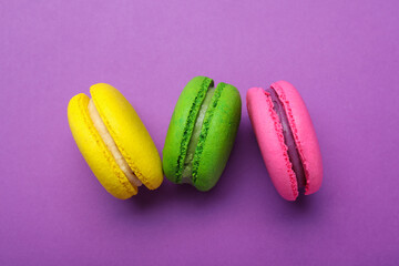 Delicious colorful macarons on purple background, flat lay