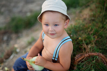 A little boy in a hat is fishing in the lake on a summer evening, peeling an onion for fish soup 