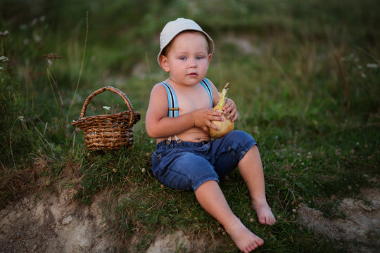 A little boy in a hat is fishing in the lake on a summer evening, peeling an onion for fish soup 
