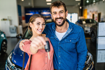 Beautiful young smiling couple holding a key of their new car.