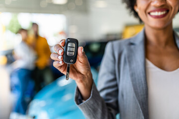 African American saleswoman holding key of new car. Customers in background.