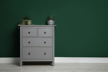 Modern chest of drawers with houseplants near green wall indoors. Space for text