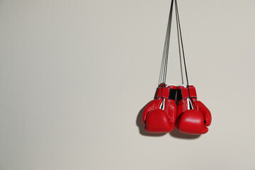 Pair of boxing gloves hanging on beige wall, space for text