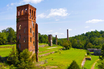 View of abandoned brick mill and smokestack with lush grass, forest