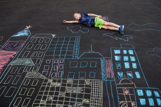 the child is lying on the asphalt. A city drawn in chalk on the asphalt