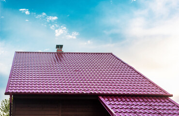 Roof of a house with a red tile roof under a clear blue sky in summer.