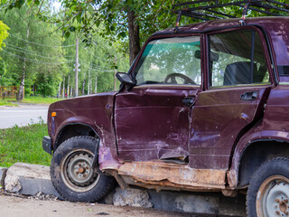 Abandoned after the accident, a purple passenger sedan. Car flew over the curb, damaged by the impact of the door close-up. Side view, without people. Concept of dangerous driving without a license.