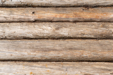 Fragment of a wooden wall of a village house. The logs lie horizontally. The wood has aged from time to time. Background Texture.