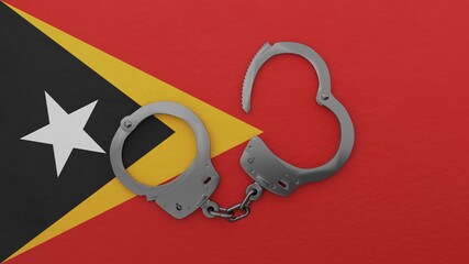 A half opened steel handcuff in center on top of the national flag of East Timor