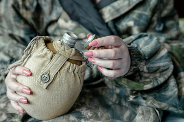 The female soldier opened the flask to drink water. Military flask in female hands. Military woman...