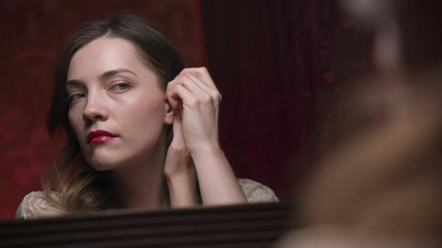 Close-up of attractive Caucasian young woman looking in the mirror, straightens her hair and pin it up with invisible hair. hair care in the bedroom.