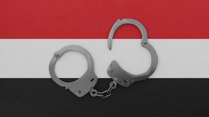 A half opened steel handcuff in center on top of the national flag of Yemen