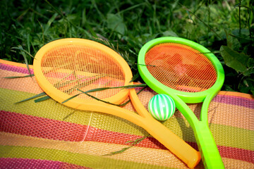 Toy tennis rackets with a ball lying on the grass. Active outdoor games in summer season