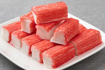Plate with whole and half red Japanese Surimi sticks close up   
