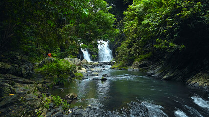 waterfall with rocks among tropical jungle with green plants and trees and water falling down into river