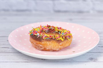 Pastries concept. Donuts with chocolate glaze with colorfull sprinkles, on a pink plate. Top view
