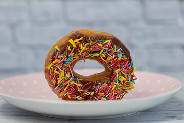 Pastries concept. Donuts with chocolate glaze with colorfull sprinkles, on a pink plate. side view